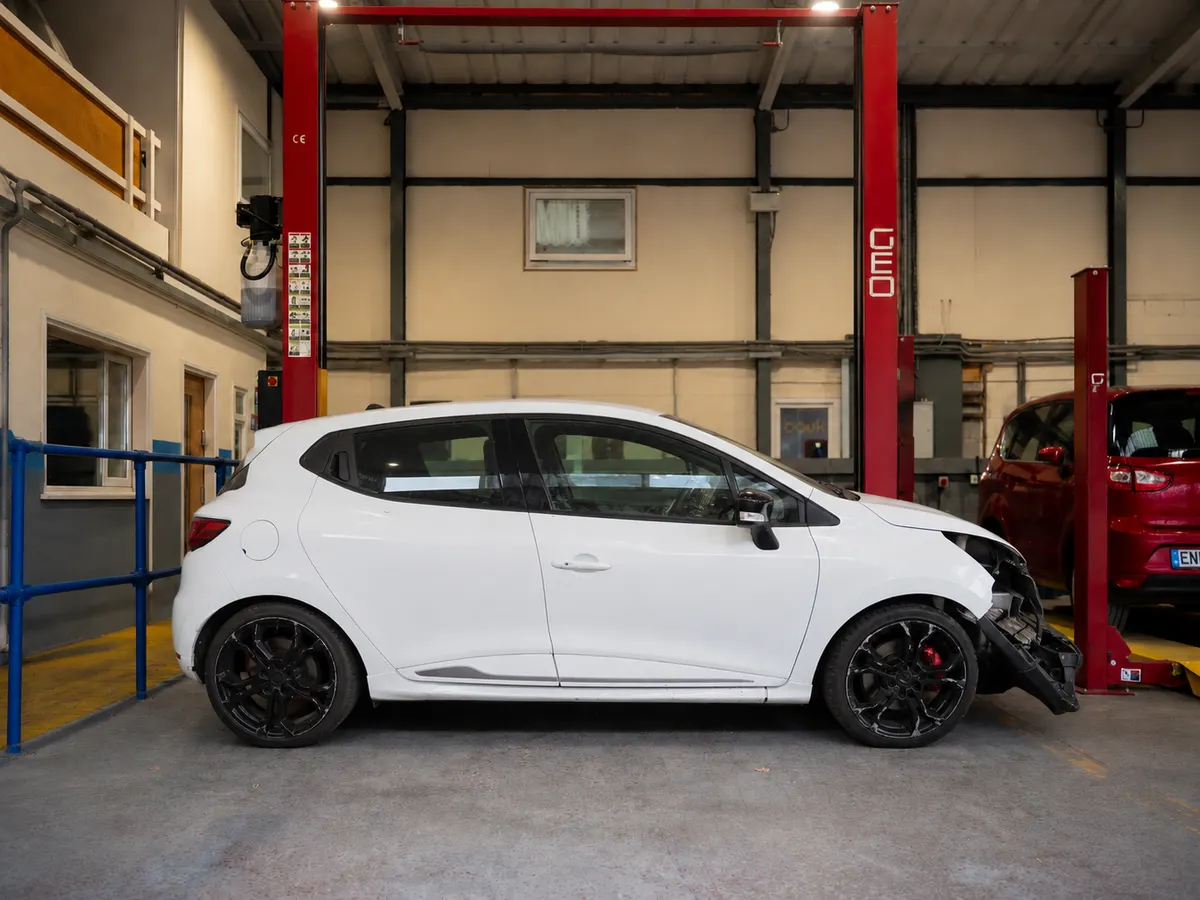White Renault Clio RS photographed side-on in a workshop, with damage to the front offside corner