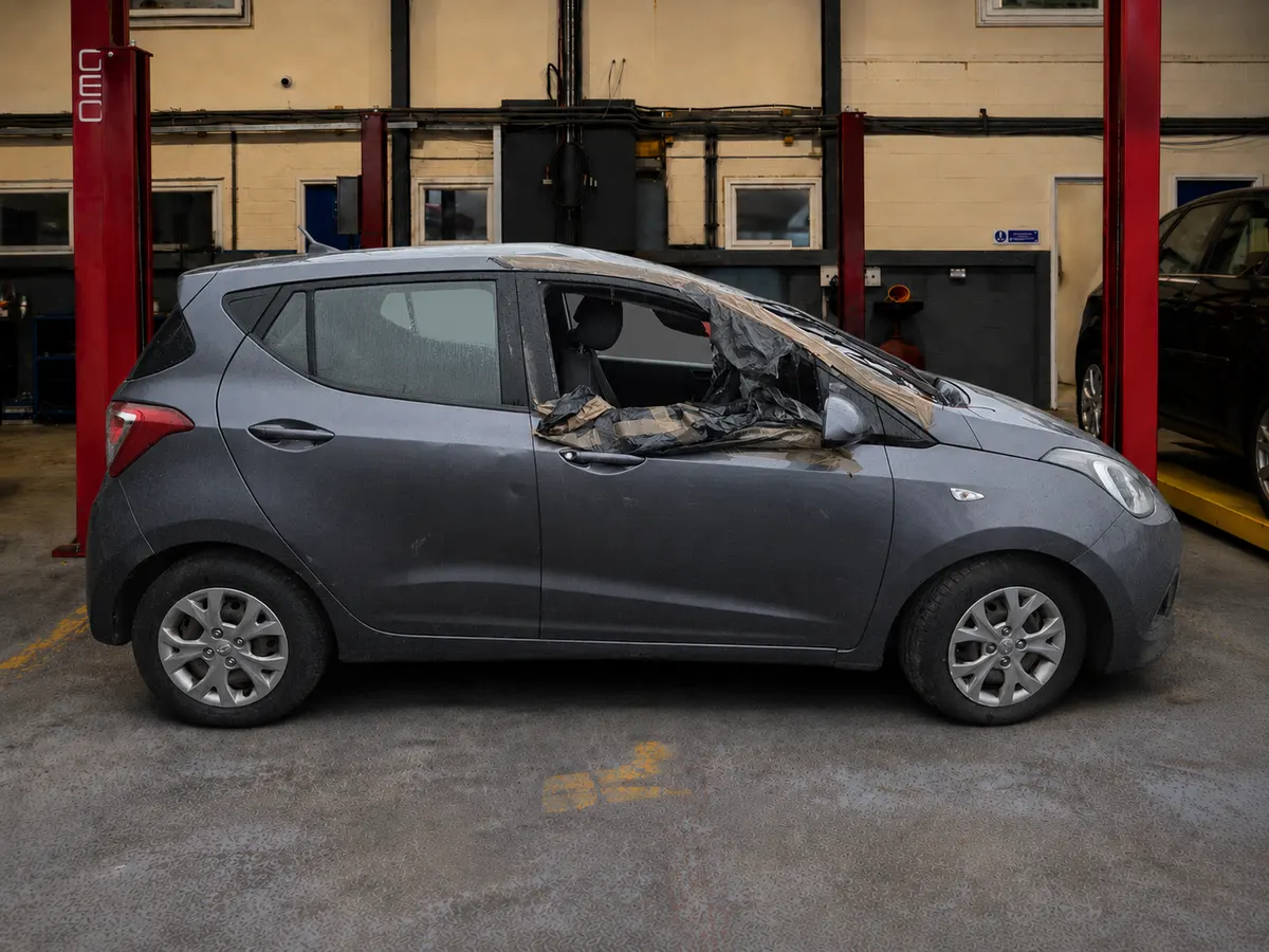 Grey Hyundai i10 raised in a workshop, its roof and nearside crushed and the windows smashed