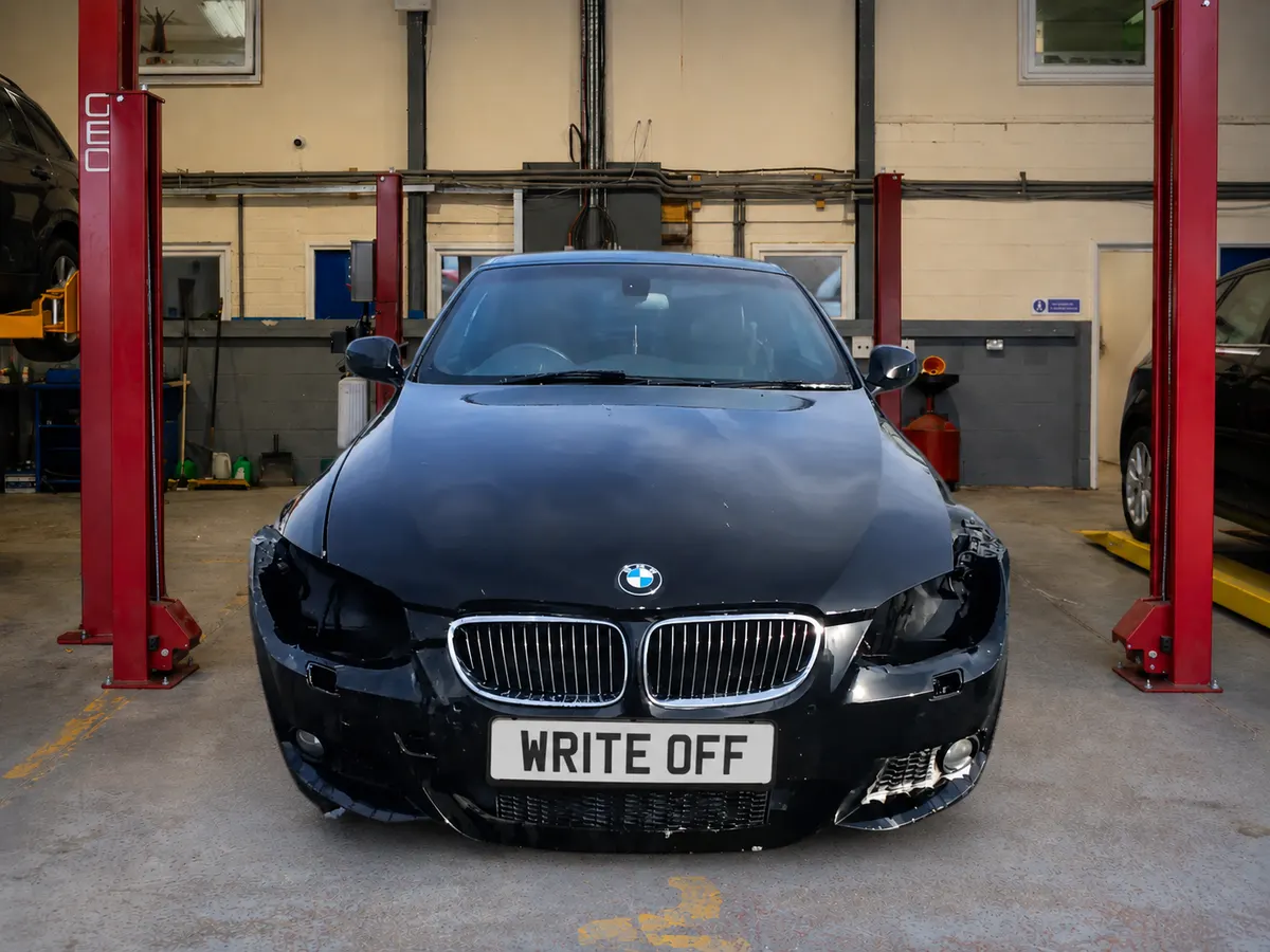 Black BMW 3 Series in a workshop with minor front-end cosmetic damage, the front structure visibly intact