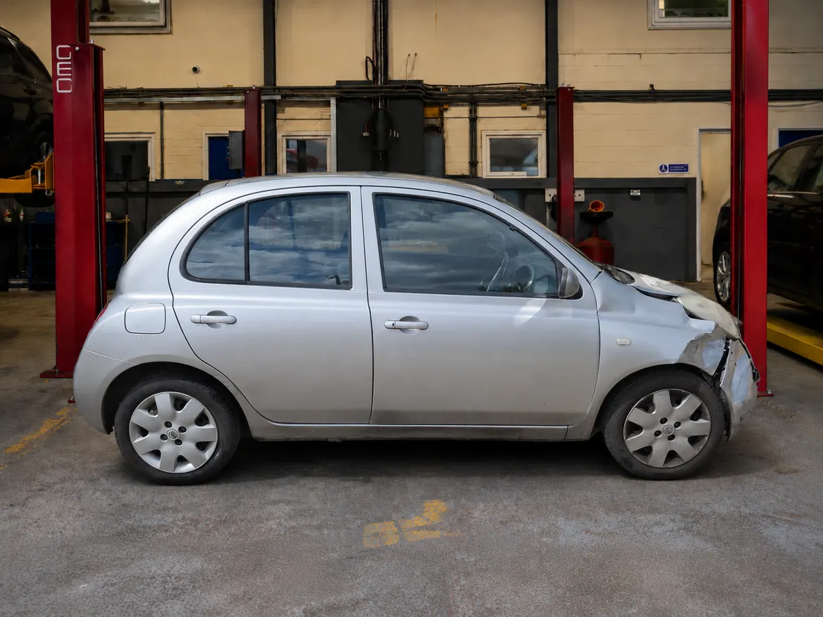 Silver Nissan Micra photographed side-on in a workshop with light damage to the front corner