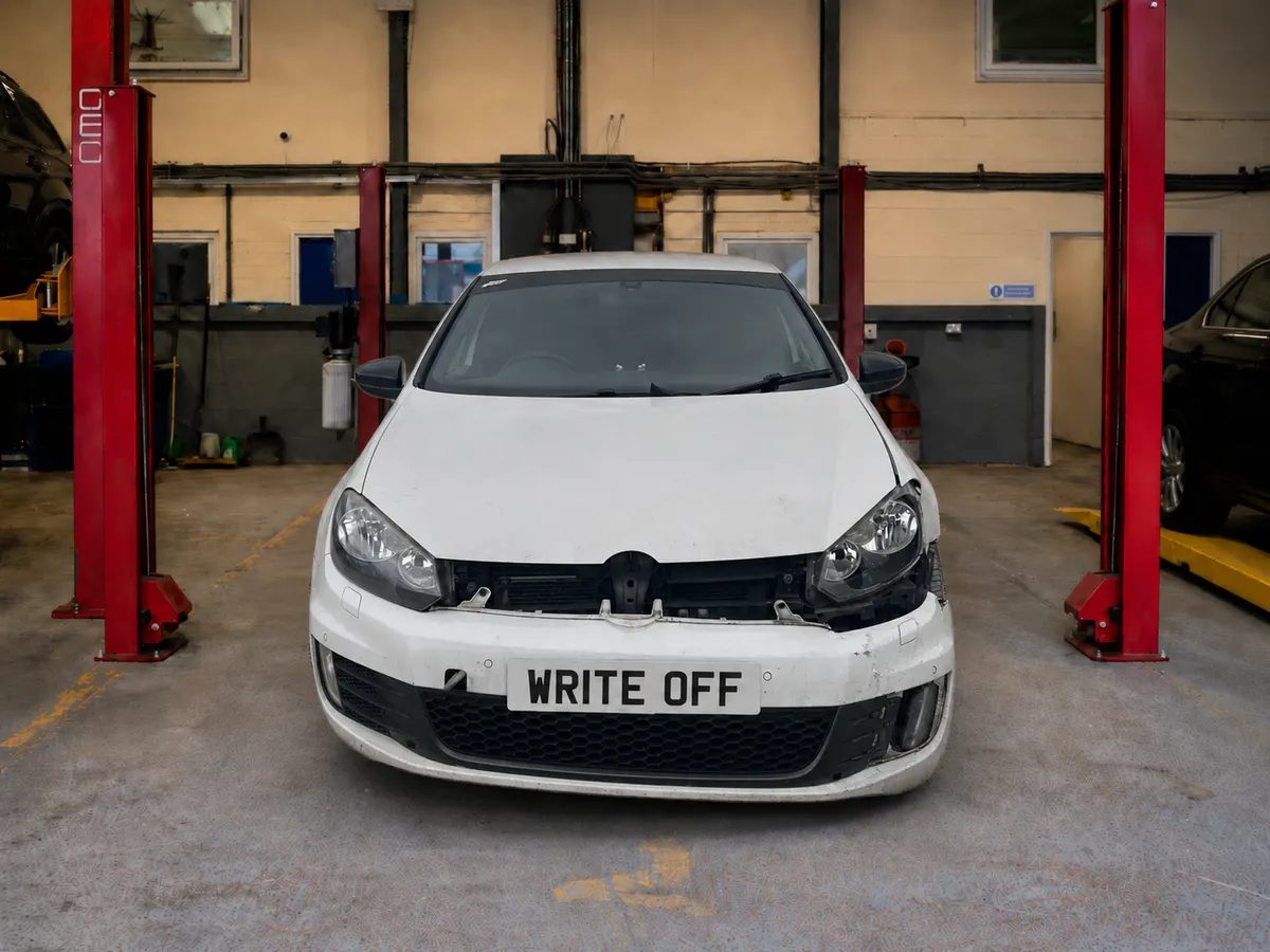 White Volkswagen Golf in a UK salvage workshop with front-end impact damage to the bumper, grille and headlight