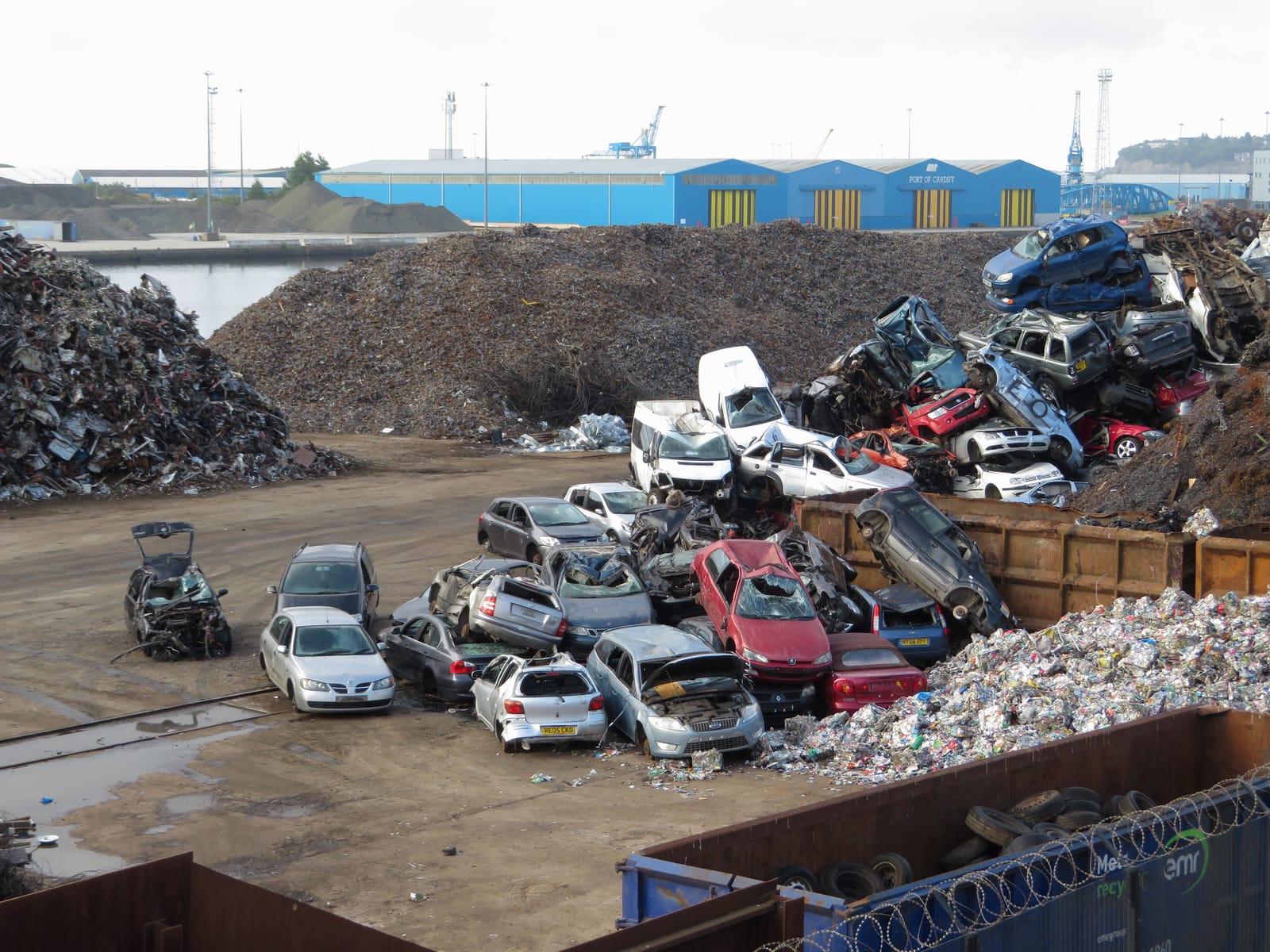 Piles of end-of-life cars stacked for scrap beside warehouses at the Port of Cardiff